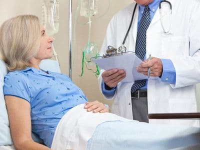 Senior woman in a hospital bed having talking to male doctor with stethoscope and clipboard